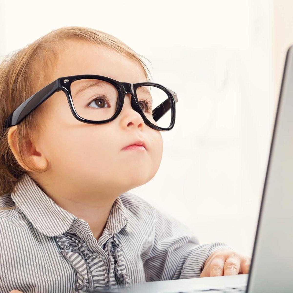 Smart little toddler girl wearing big glasses while using her laptop