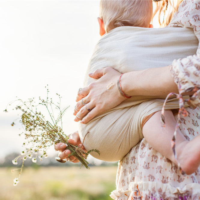 Mother is holding and tickling her baby, babywearing in sling
