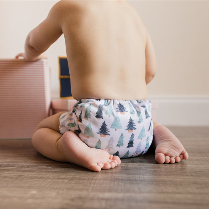 An 11-Month-Old Christmas Baby Boy with 12 Toes Wearing a Sustainable Christmas Cloth Diaper Sitting on a Wooden Floor Playing with Christmas Presents