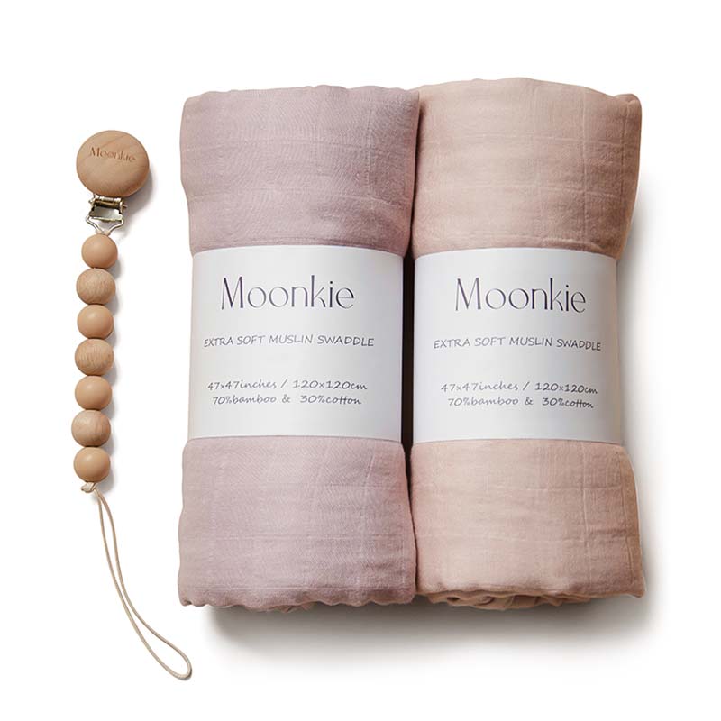 Two folded Muslin swaddle blankets in blush/soft mauve color with a silicone pacifier clip, all displayed on a neutral background.