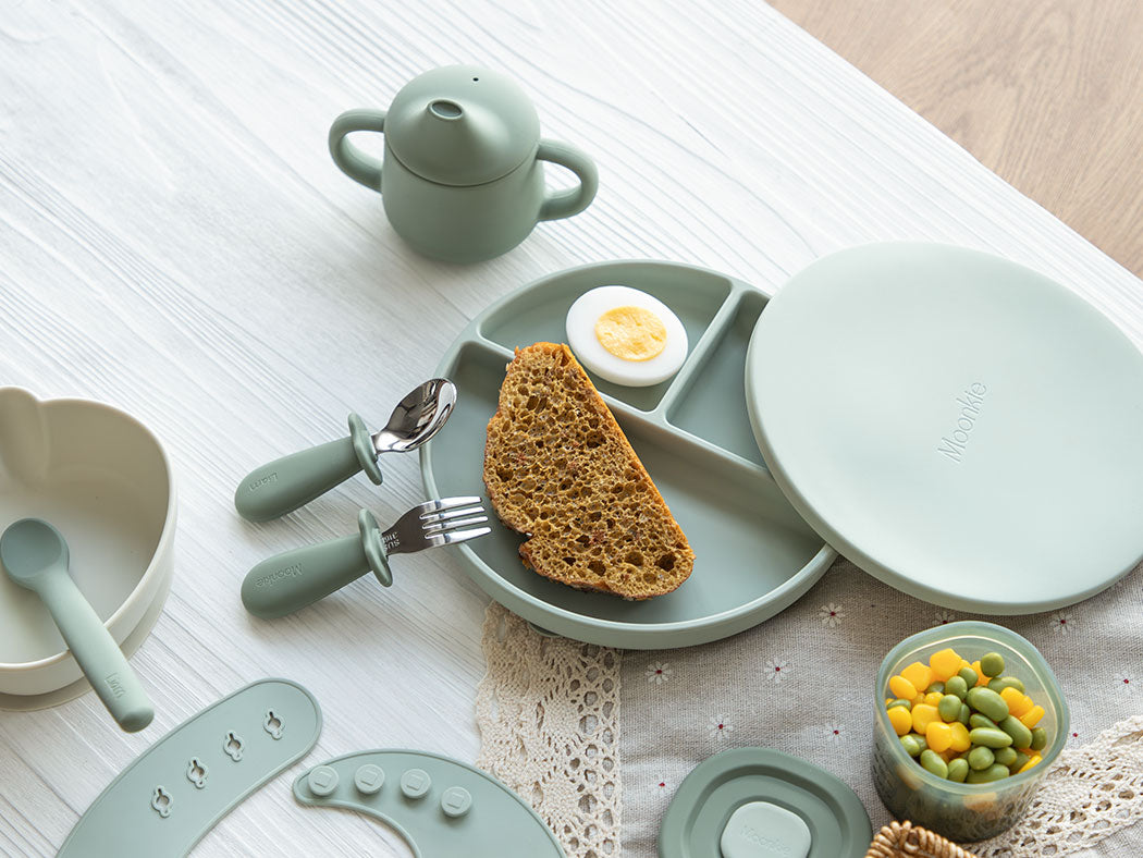 Children's tableware set with plate, bowl, and cutlery on a light surface.