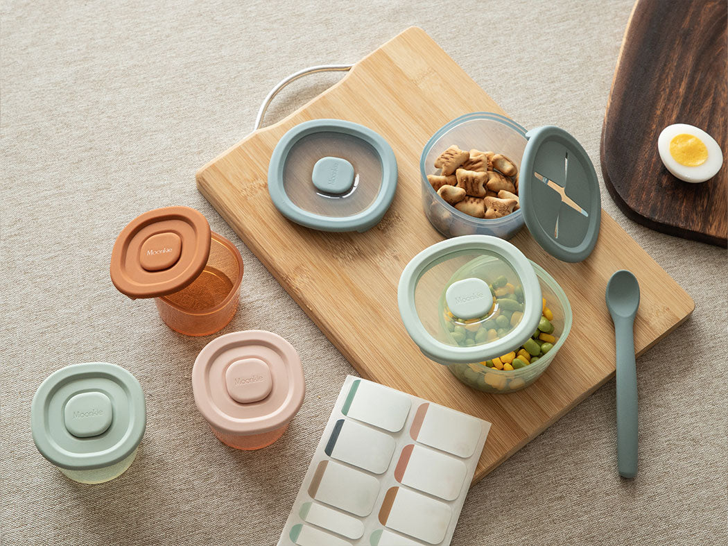 Set of colorful food containers on a wooden board with a neutral background