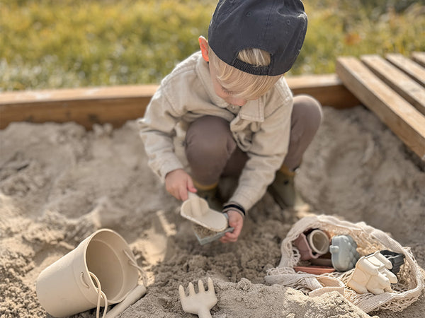 Child playing in a sandbox with toys and a cap
